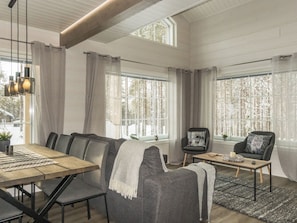 Una sala de estar moderna con comedor, ventanas amplias con cortinas y vistas a un paisaje nevado.