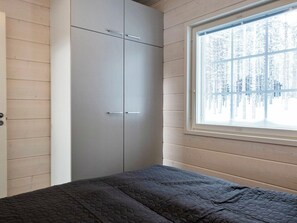 Een slaapkamer met een bed, een kledingkast en een raam met uitzicht op een besneeuwd bos.