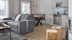 A modern living room with a grey sofa, wooden dining table, and a kitchen with stainless steel appliances.