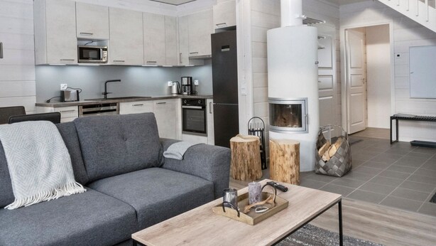 A modern living room with a grey sofa, a coffee table with decorative items, and a kitchen area with white cabinets and appliances.