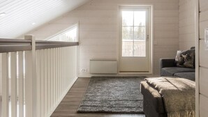 A loft-style room with a sloped ceiling, a large window, a radiator, a gray sofa, and a dark rug.