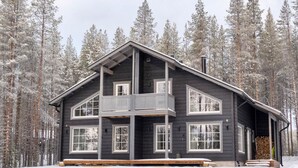 A two-story log cabin with a balcony, surrounded by a snowy forest.