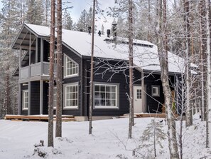 Une cabane à deux étages dotée d’un balcon, entourée d’arbres couverts de neige.