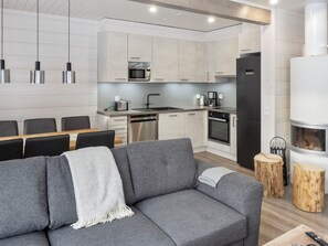 Eine moderne Küche mit Edelstahlgeräten, eine Essecke mit grauem Sofa und ein eingebauter Holzofen.