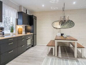 Une cuisine moderne avec des meubles de couleur sombre, un plan de travail en bois et un coin repas comprenant un banc et une table.
