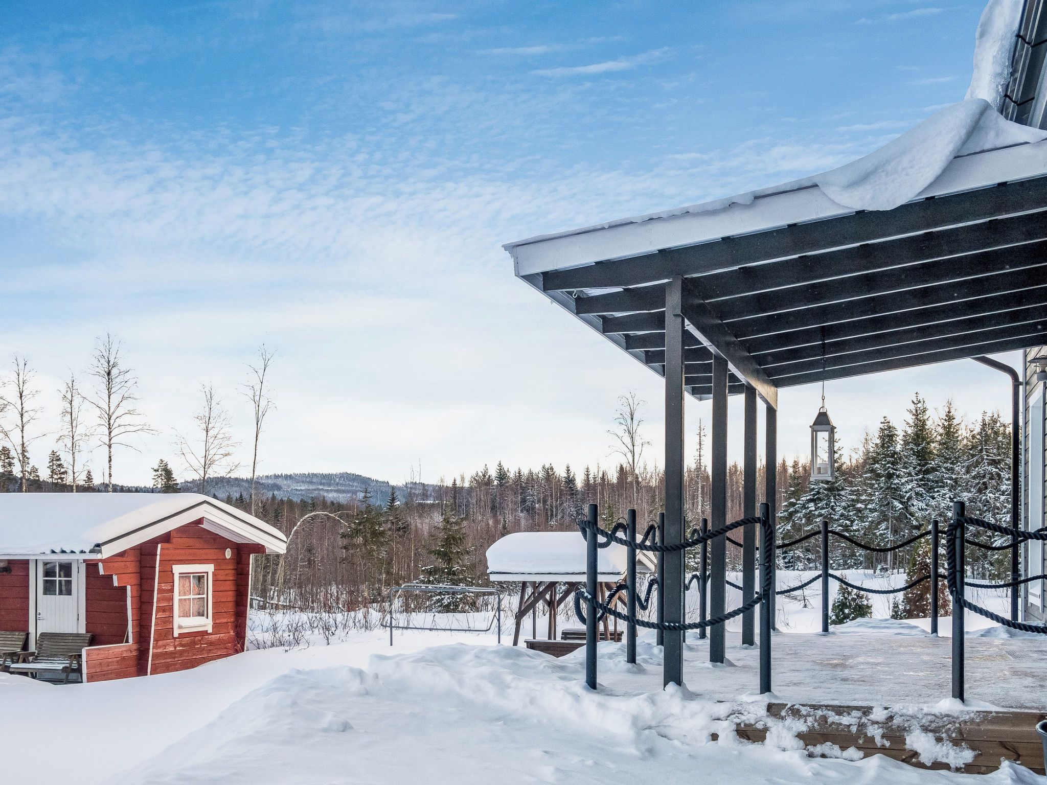 Una cabaña de madera con un espacio exterior cubierto, rodeada de árboles nevados y un cielo despejado.