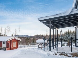 Une cabane en bois dotée d’un espace extérieur abrité, entourée d’arbres couverts de neige et surplombant un ciel dégagé.