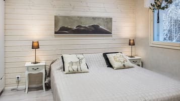 Un dormitorio con cama, dos mesitas de noche, un aparador, un cuadro en la pared y una ventana con vistas a árboles.