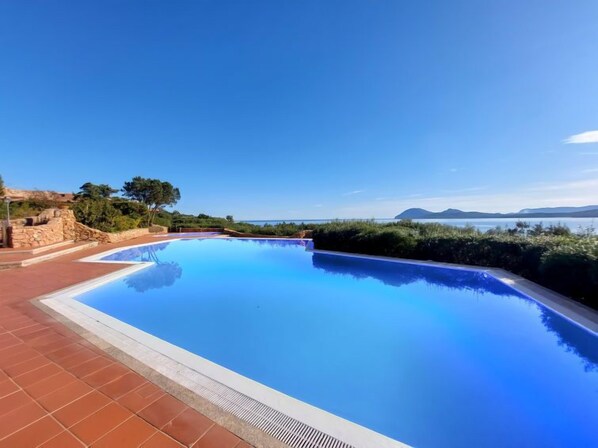 A clear blue swimming pool with a view of the sea and mountains in the background.