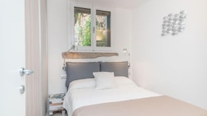 A bedroom with a bed, a window with a view of greenery, a bedside table with a lamp, and a wall-mounted light fixture. - La Nina by Interhome (Porto Rotondo)