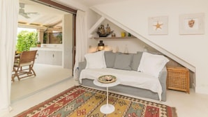 A cozy living room with a gray sofa, a small round table, and a colorful rug. There is a kitchen visible through an open door, and a staircase leading to an upper level. - La Nina by Interhome (Porto Rotondo)