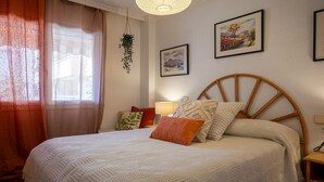 Ein Schlafzimmer mit einem großen Bett, einer hängenden Pflanze und zwei gerahmten Bildern an der Wand.