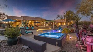 Un área de piscina moderna al aire libre con sillones de descanso y un jacuzzi, rodeada por un jardín ajardinado.