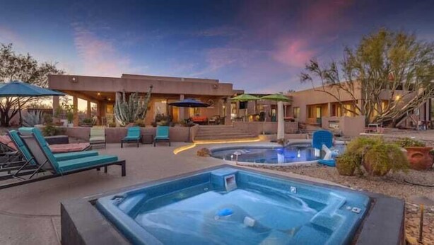 Un área de hidromasaje con sillones de descanso y sombrillas, una piscina y un edificio con terraza.