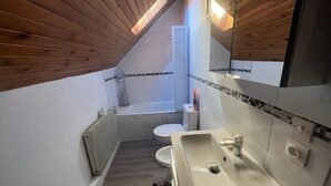 Un baño pequeño y funcional con techo de madera, un lavamanos blanco, inodoro y bañera.