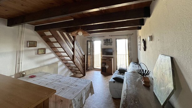 Una habitación espaciosa con techo de madera, una escalera, una mesa de comedor, un sofá y un televisor.