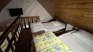 Un dormitorio abuhardillado pequeño, con paneles de madera, equipado con dos camas individuales, un banco de madera y un televisor de pantalla plana montado en la pared.