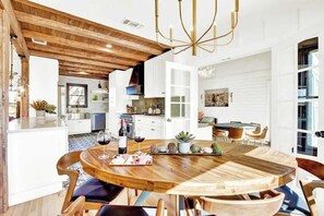 A modern kitchen with white cabinets, a wooden dining table, and a chandelier. - Ruth's Place - Walk to Main, Hot Tub & Fire Pit (Fredericksburg)