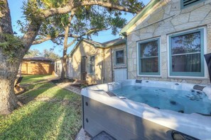 A backyard with a hot tub, stone house, and a large tree. - Ruth's Place - Walk to Main, Hot Tub & Fire Pit (Fredericksburg)