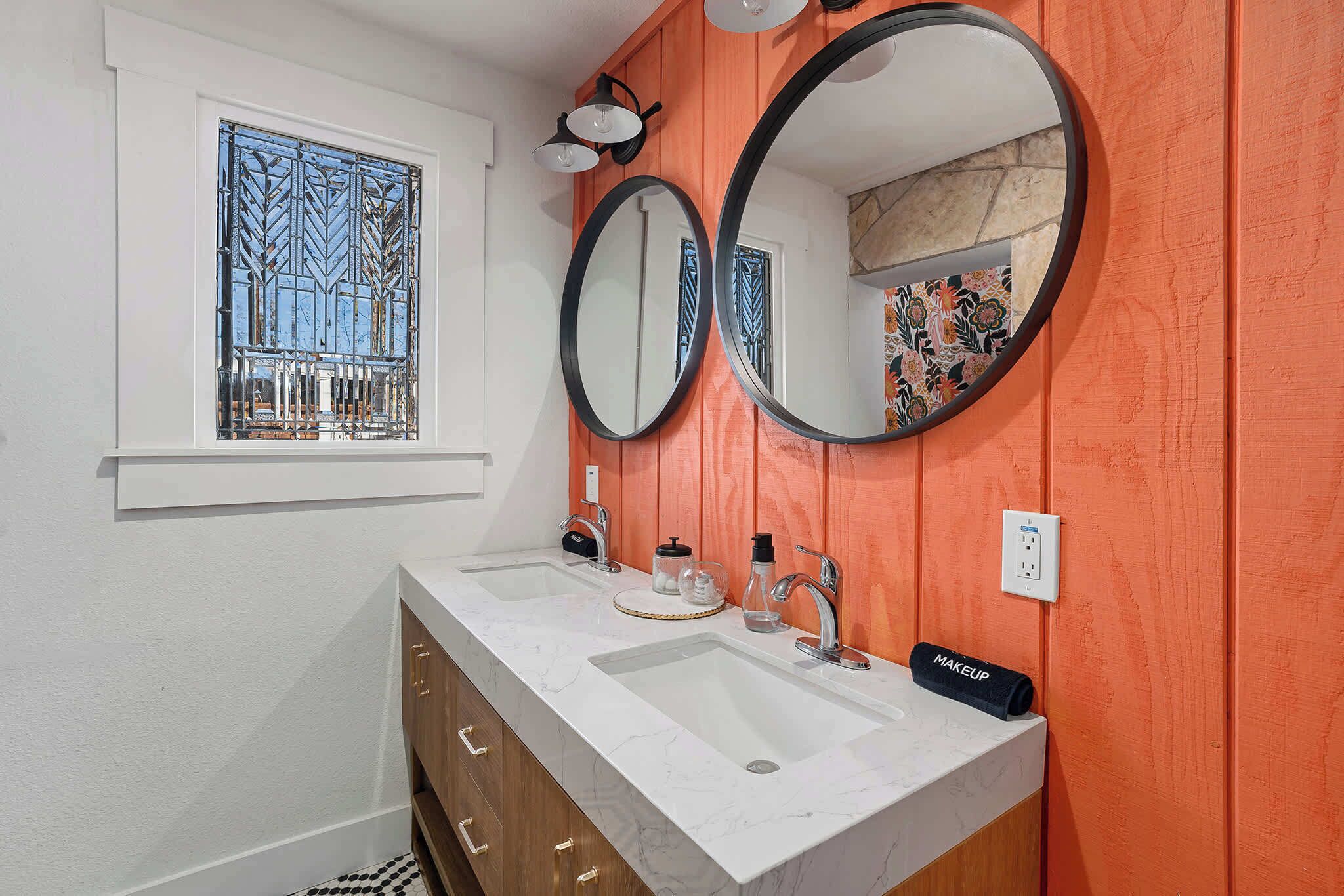 A bathroom with two sinks, a window with a decorative metal grille, and a mirror with a black frame.