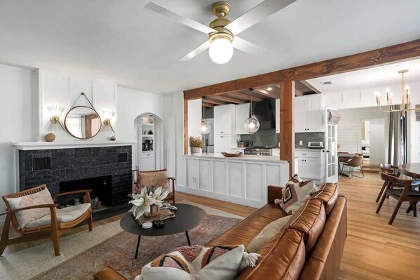 A modern living room with a fireplace, a dining area, and a kitchen in the background. - Ruth's Place - Walk to Main, Hot Tub & Fire Pit (Fredericksburg)