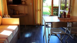 Een knus ingerichte kamer met een bed, een bureau, een stoel en een tafel. Er is een raam met gordijnen, een lamp op het bureau en een fles op de tafel.
