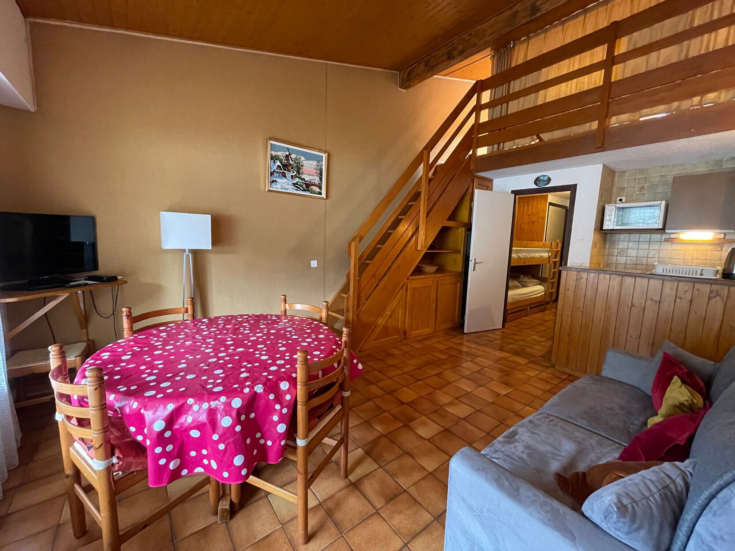 A compact living space with a dining table, a sofa, a kitchen area, and a staircase.