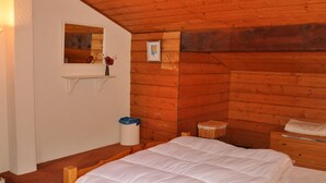 Une chambre confortable avec un plafond en bois, un lit recouvert d’une literie blanche, une petite étagère avec un vase et un tableau encadré au mur.