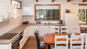 Eine moderne Küche mit weißen Schränken, einem Holzespeisetisch und Blick auf den Wald durch ein großes Fenster.