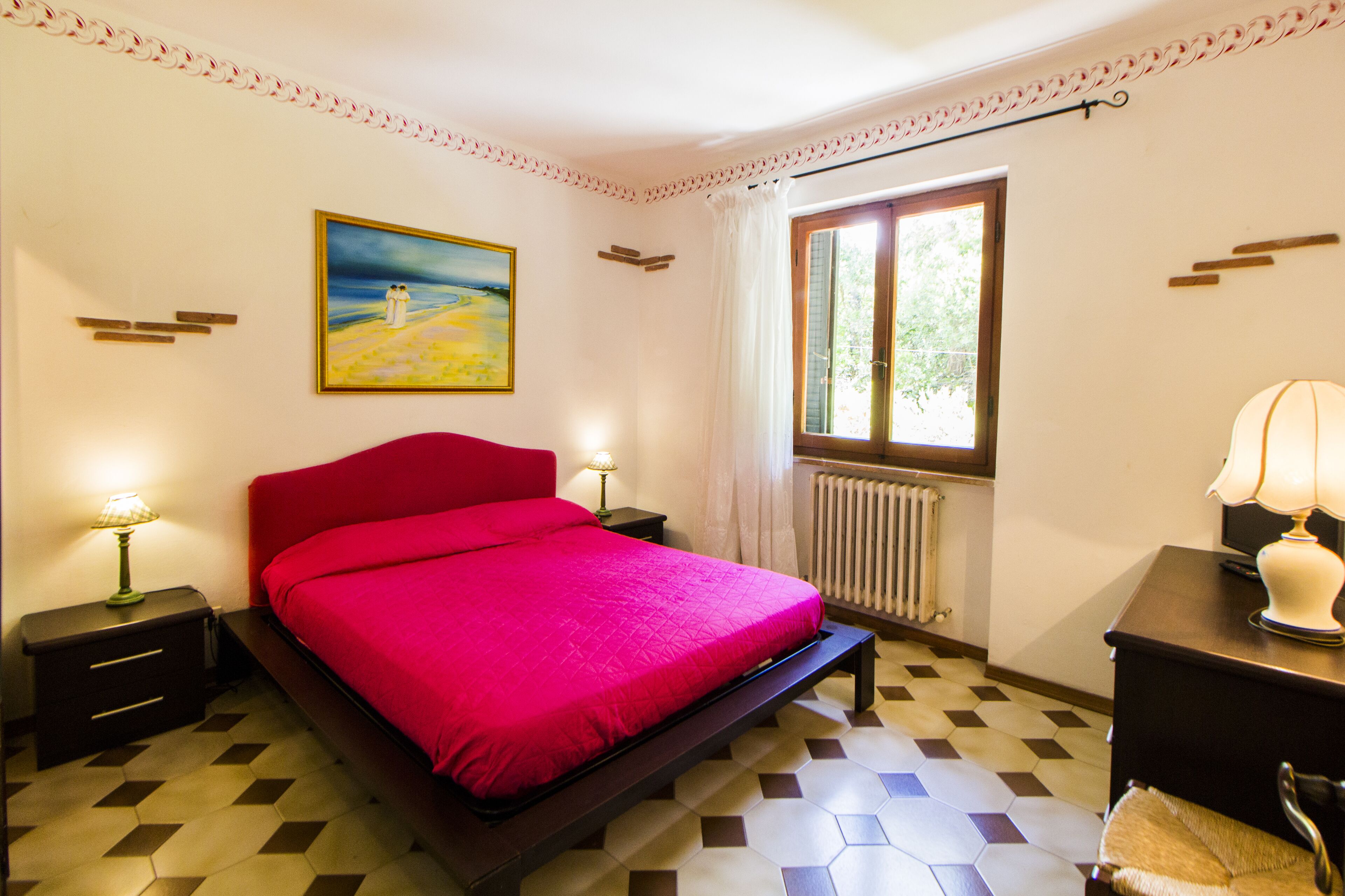 Ein Schlafzimmer mit einem Bett, Nachttischen, einem Fenster und einem Bild an der Wand.