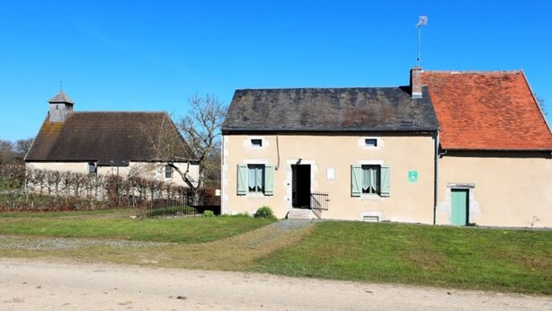 Un bâtiment à deux étages, avec un chemin de terre menant à l’entrée, un petit porche et une cheminée.