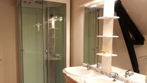 Une salle de bain dotée d’une douche à parois de verre, de deux vasques avec des plans de travail en marbre et d’un miroir muni d’un porte-serviettes.