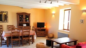 Un salon chaleureux comprenant un coin repas, des meubles en bois, un téléviseur et une fen être laissant entrer la lumière naturelle.