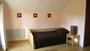 Une chambre avec un lit en bois, une petite table de chevet et un radiateur. Trois tableaux encadrés sont accrochés au mur.
