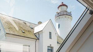 Un edificio blanco con una torre de techo rojo, posiblemente un faro, y una ventana con vista al cielo.