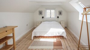 Un dormitorio con una cama grande, una mesa de madera, un escritorio pequeño, un radiador y un tragaluz.