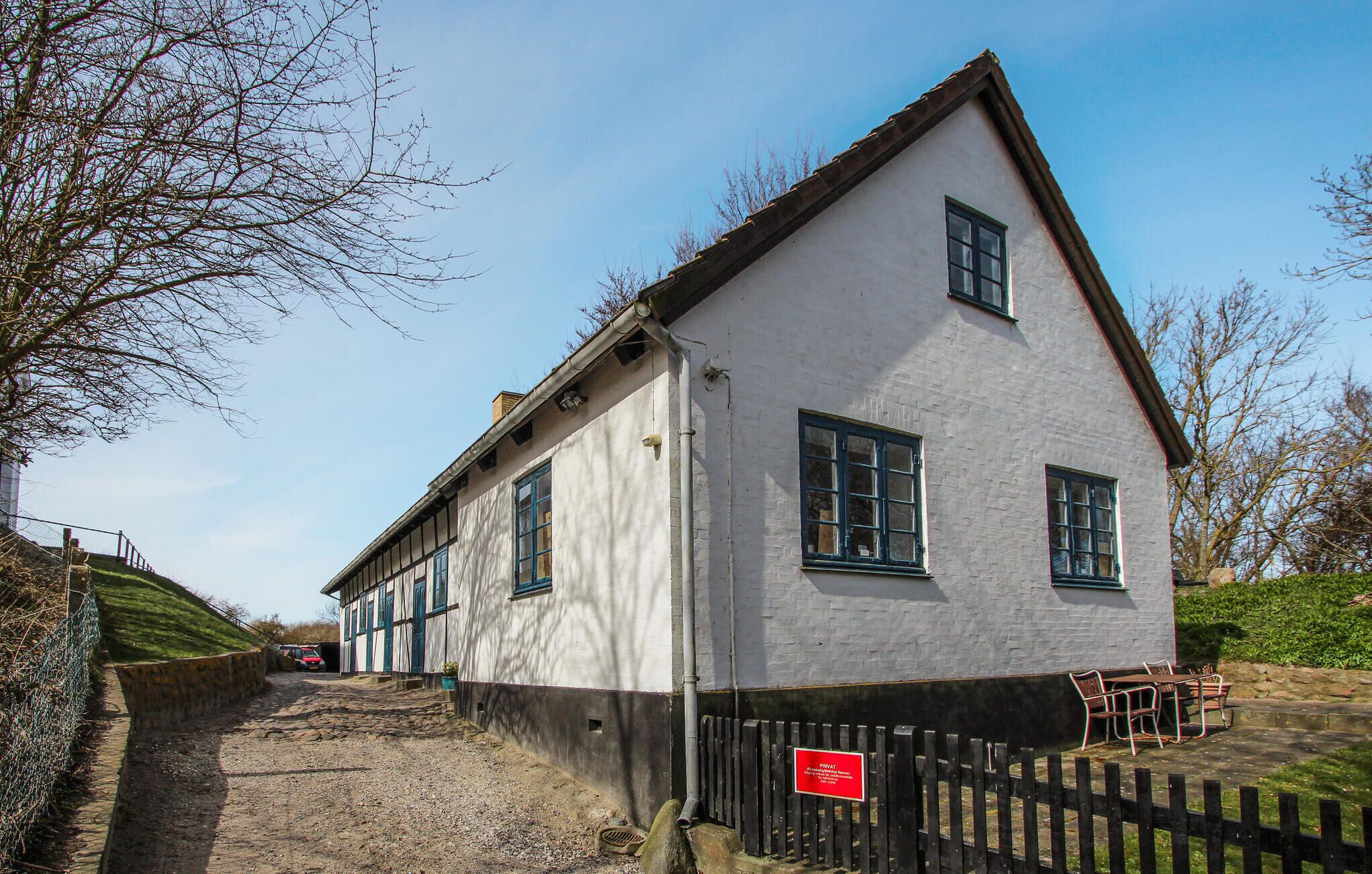 A two-story building with a white facade and dark trim, featuring a small window and a door.