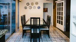 Un'area pranzo con una porta in vetro che dà su un patio, una ventola a soffitto e un pavimento piastrellato.