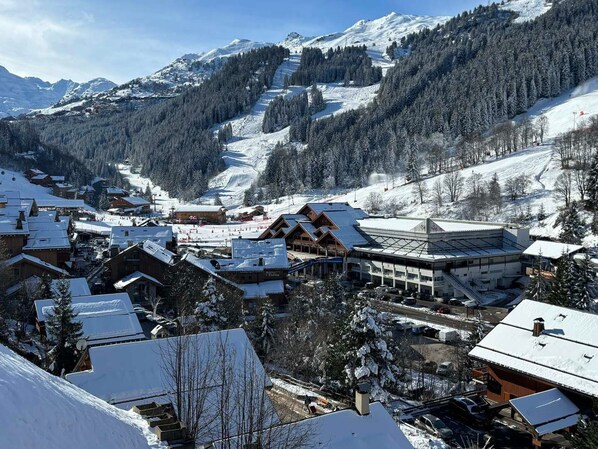 A snow-covered mountain town with traditional wooden buildings, a ski slope, and a clear view of the surrounding mountains.
