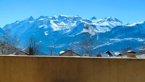 Une vue de montagnes enneigées sous un ciel dégagé, avec un mur brun au premier plan et une antenne parabolique.