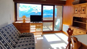 Une pièce comprenant un canapé, un téléviseur, des meubles en bois et offrant une vue sur les montagnes par le biais d’une grande fenêtre.