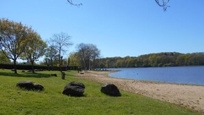 A lakeside park with grassy areas, large rocks, and trees.