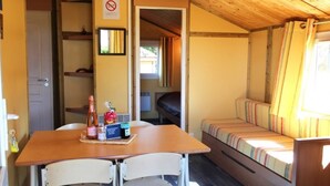 A compact room with a wooden ceiling, a bed with striped bedding, a table with chairs, and a small kitchenette area.