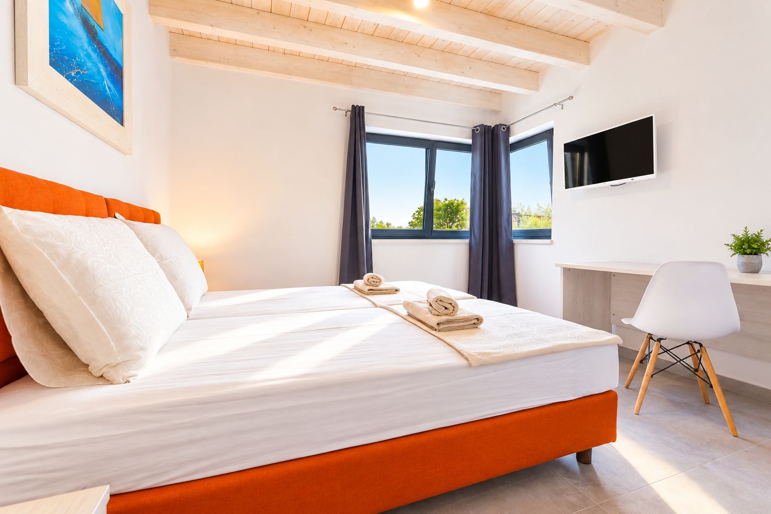 A modern hotel room with a large bed, a desk, a chair, and a TV on the wall.