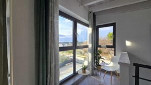 Una habitación moderna con ventanas amplias, una silla blanca, una mesita con una planta y una lámpara.