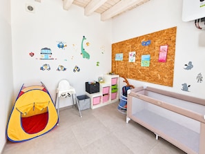 A child's playroom with a tent, a high chair, a crib, and wall decals.