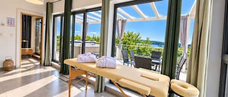 A spa room with a massage table, towels, and a view of the sea.