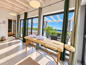 A spa room with a massage table, towels, and a view of the sea.