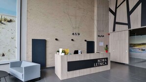 A reception desk with a sign reading "NOWA LETNICA" in a modern interior with a brick wall, a large window, and a minimalist design.