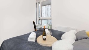A neatly made bed with a wine bottle and glasses on a tray, a towel, and a fluffy pillow.
